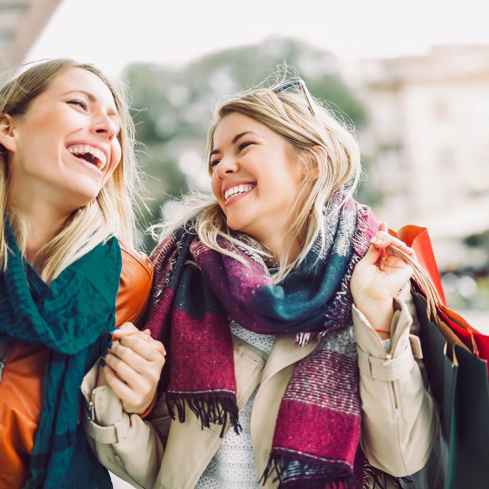Two female friends smiling while outside shopping